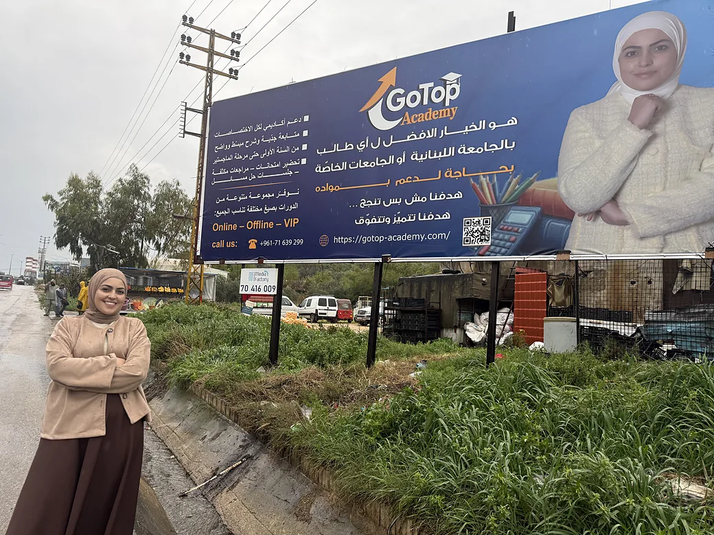 The GoTop Academy billboard on the main road, with a member of the team standing in front of it.